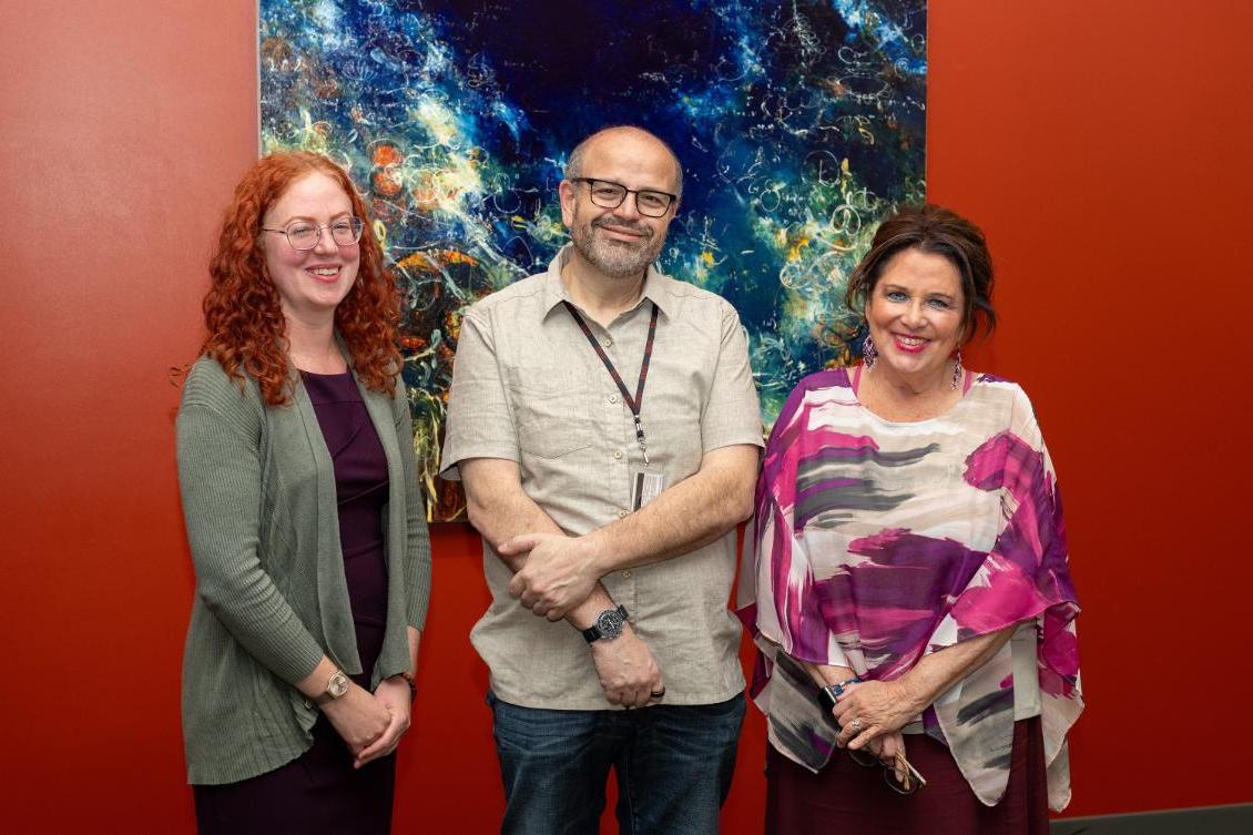 Photography of Rodriguez, Benanti, and Imanaka. The background is a red wall and a painting with blue and green colors.